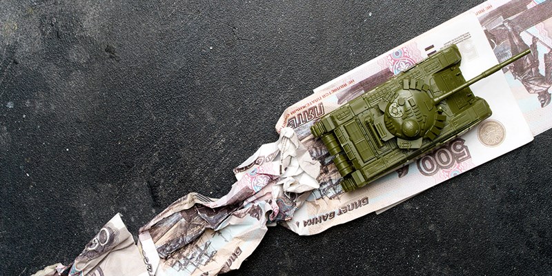 Economic crisis in Russia concept. Toy military tank on Russian rubles. War conflict in Ukraine, economic sanctions and inflation in Russia.