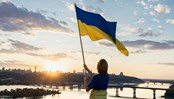 Sunset over the city of Kyiv. a woman holds a large waving Ukrainian flag standing high on the roof. Ukrainians are against war. Drawing attention to military actions in Ukraine. independence Day.